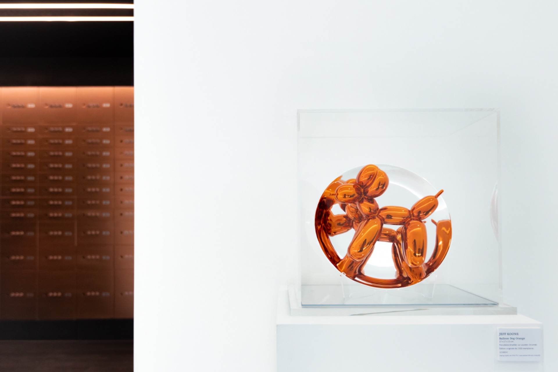 The Vault — Jeff Koons « Balloon Dog Orange » sous cloche, devant le mur cuivré du coffre-fort